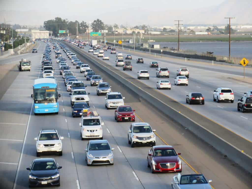 A busy highway with multiple lanes of traffic and a blue bus in the left lane.