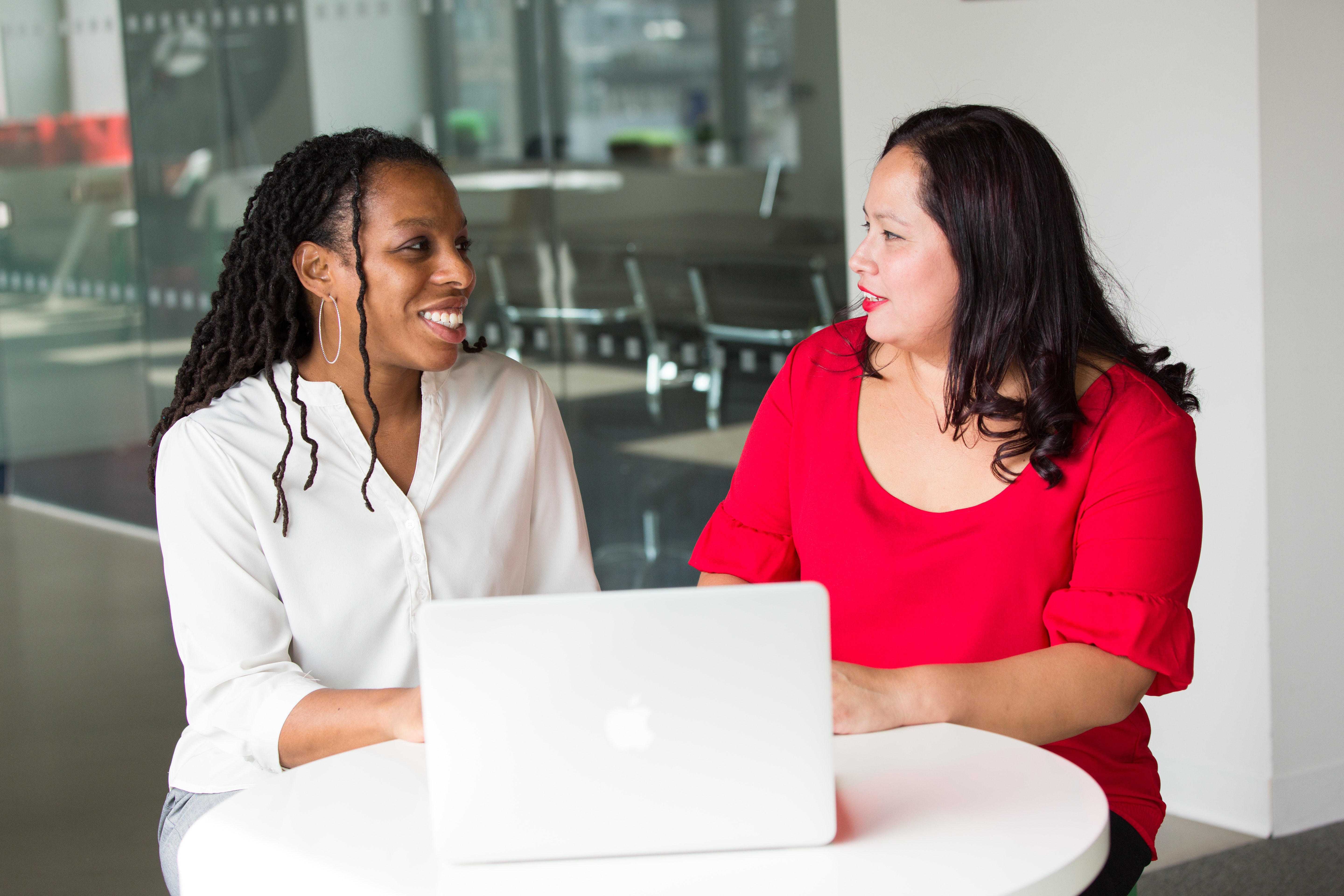 A woman and a woman having a discussion at a table with a laptop in a modern office setting.