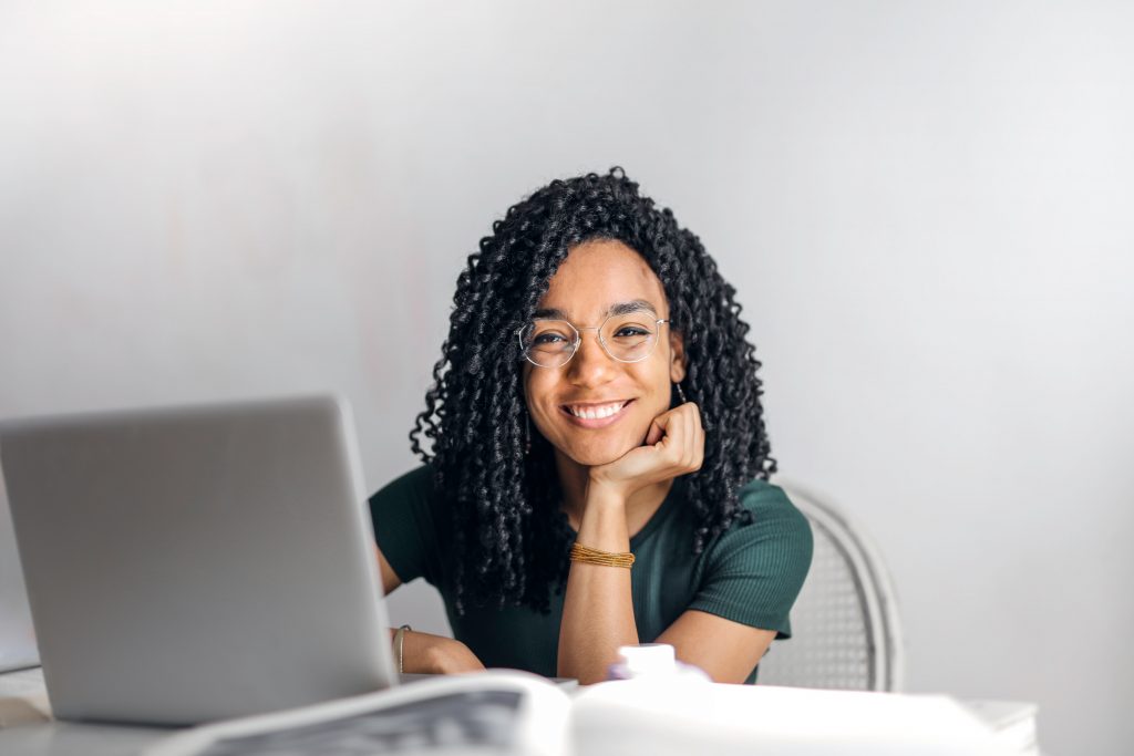 A smiling woman working on a laptop at her desk in an office setting.