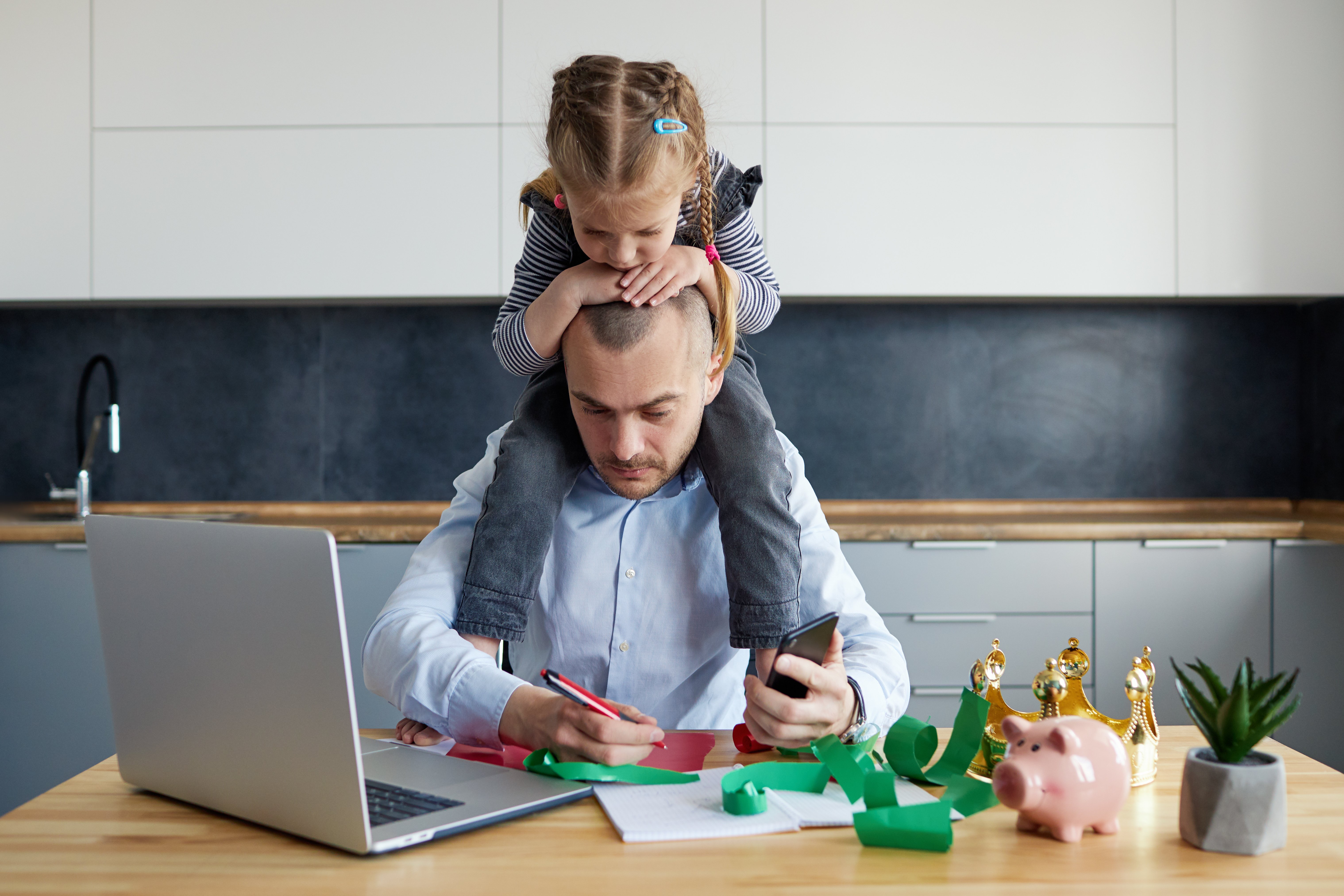 A father and daughter playing with toy chess pieces at a desk in a modern kitchen.