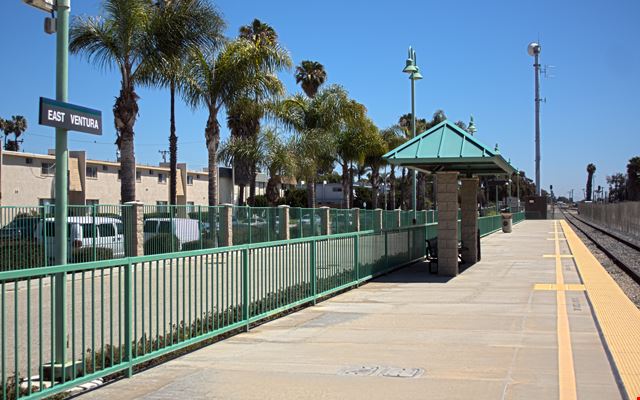 East Ventura train station platform with palm trees and shelter, sunny day.