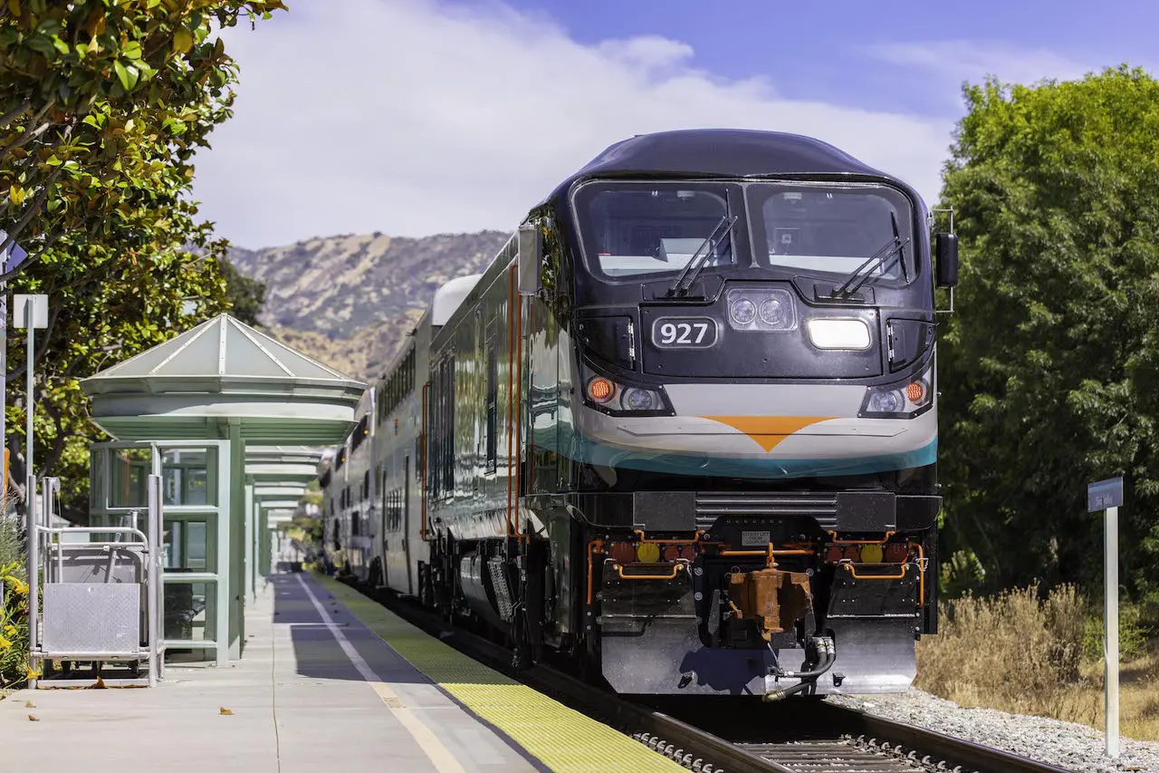 A modern commuter train at Goventura Staging station with scenic mountain background.