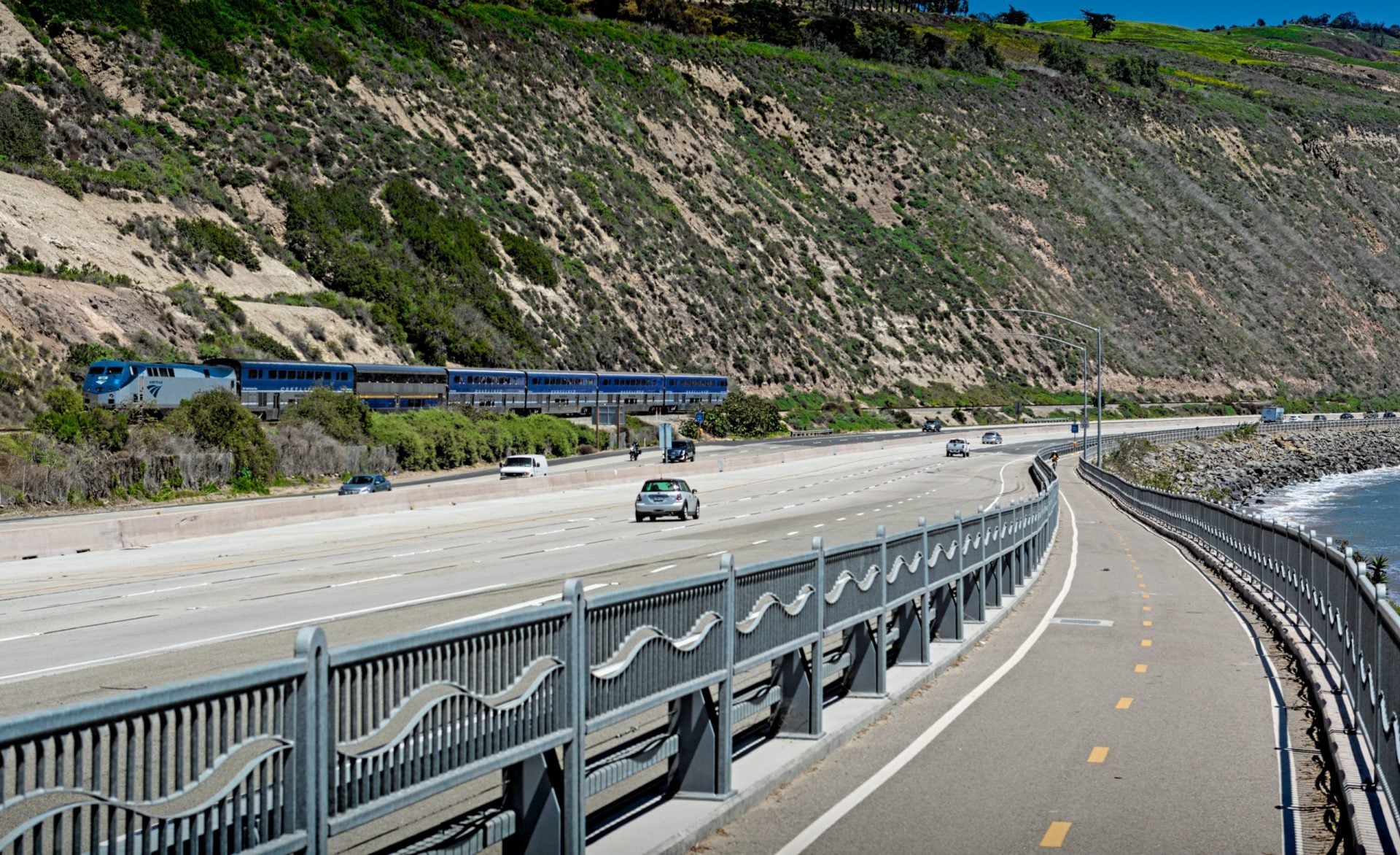 Train running next to Highway 1 with bike path next to beach