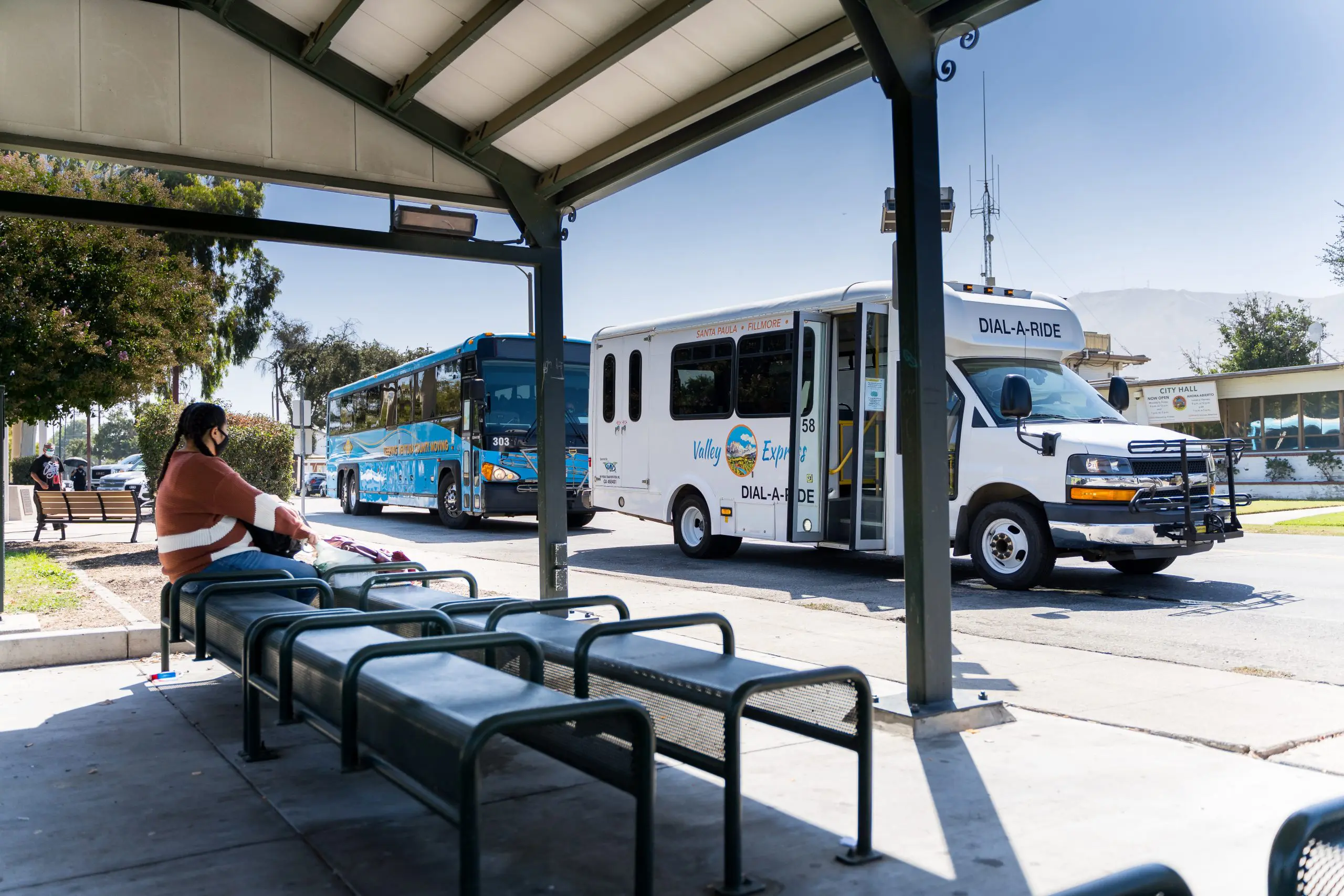 A bus stop with a woman sitting on a bench, waiting for the bus in Ventura.