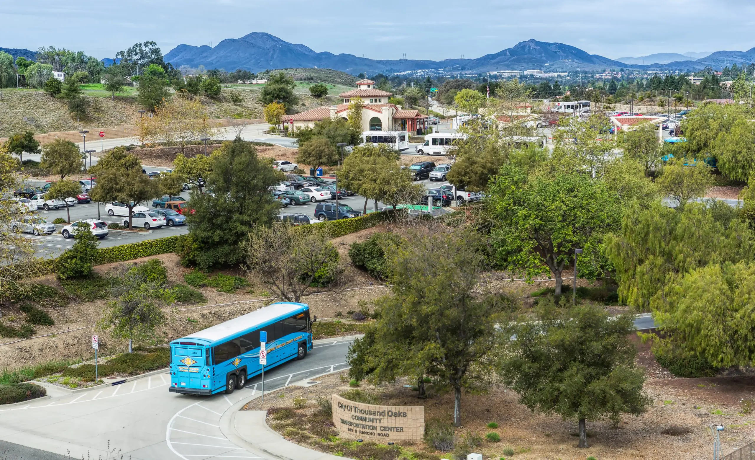 A blue bus parked in a scenic area with trees and mountains in the background at Goventura Staging.