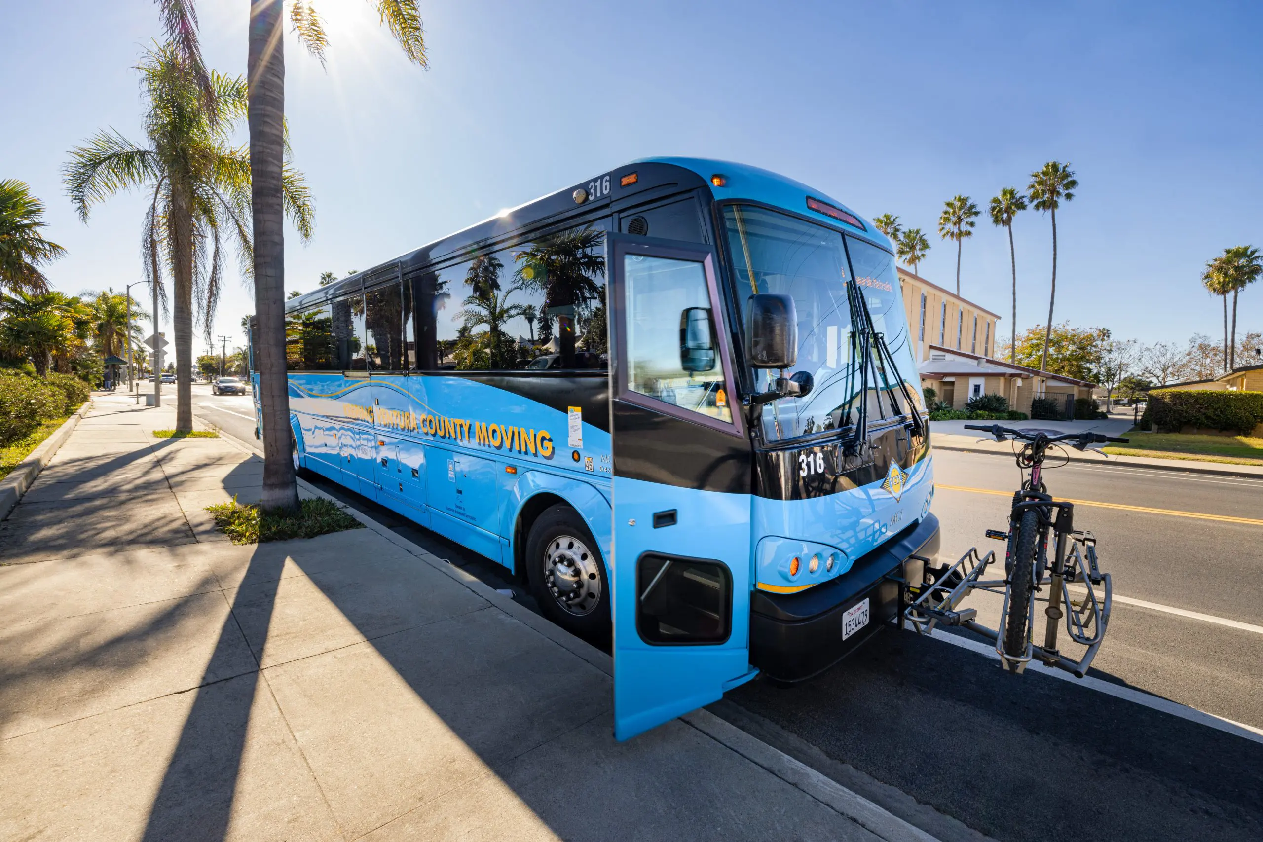 Modern blue shuttle bus parked on sunny street with palm trees in Ventura.