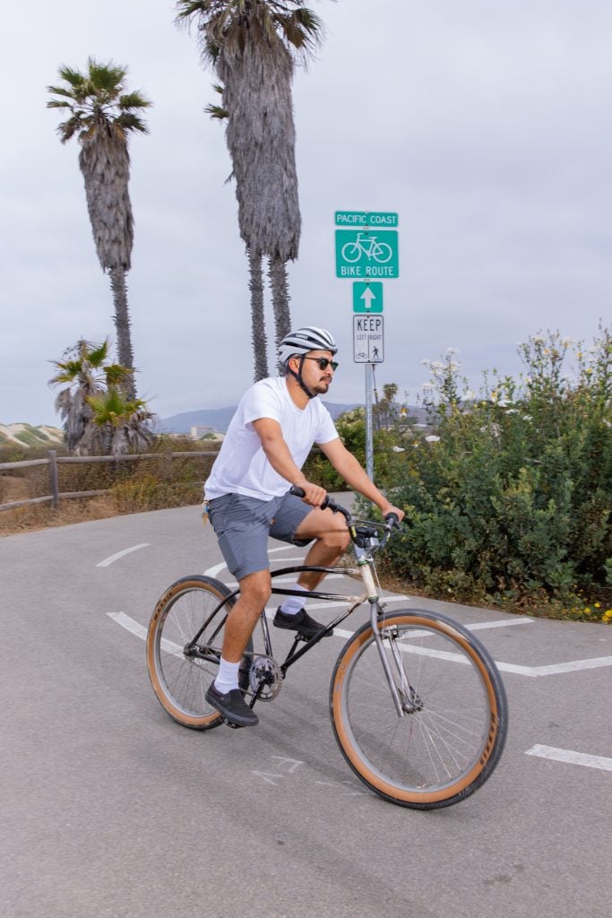A cyclist riding on a designated bike route along the Pacific Coast with palm trees in the backgroun.
