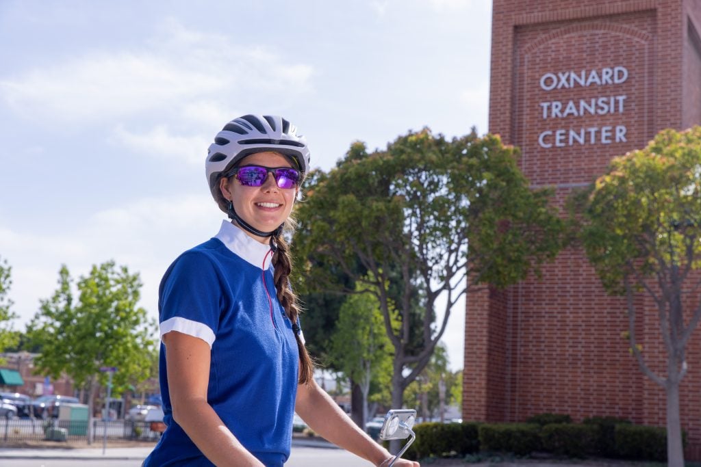 A woman cyclist smiling in front of Oxnard Transit Center during daytime.