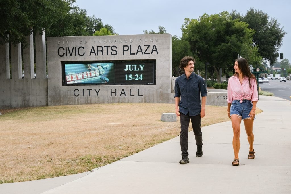 A young man and woman walking past Civic Arts Plaza sign in Thousand Oaks, California.