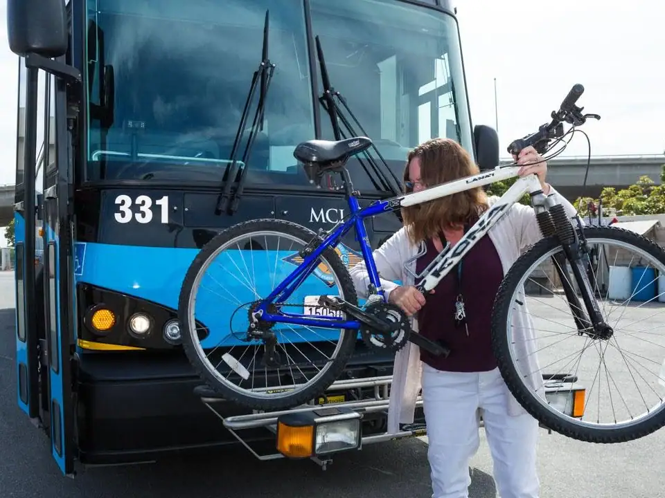 A woman loading a bicycle onto a bus at Goventura Staging, urban transit scene.