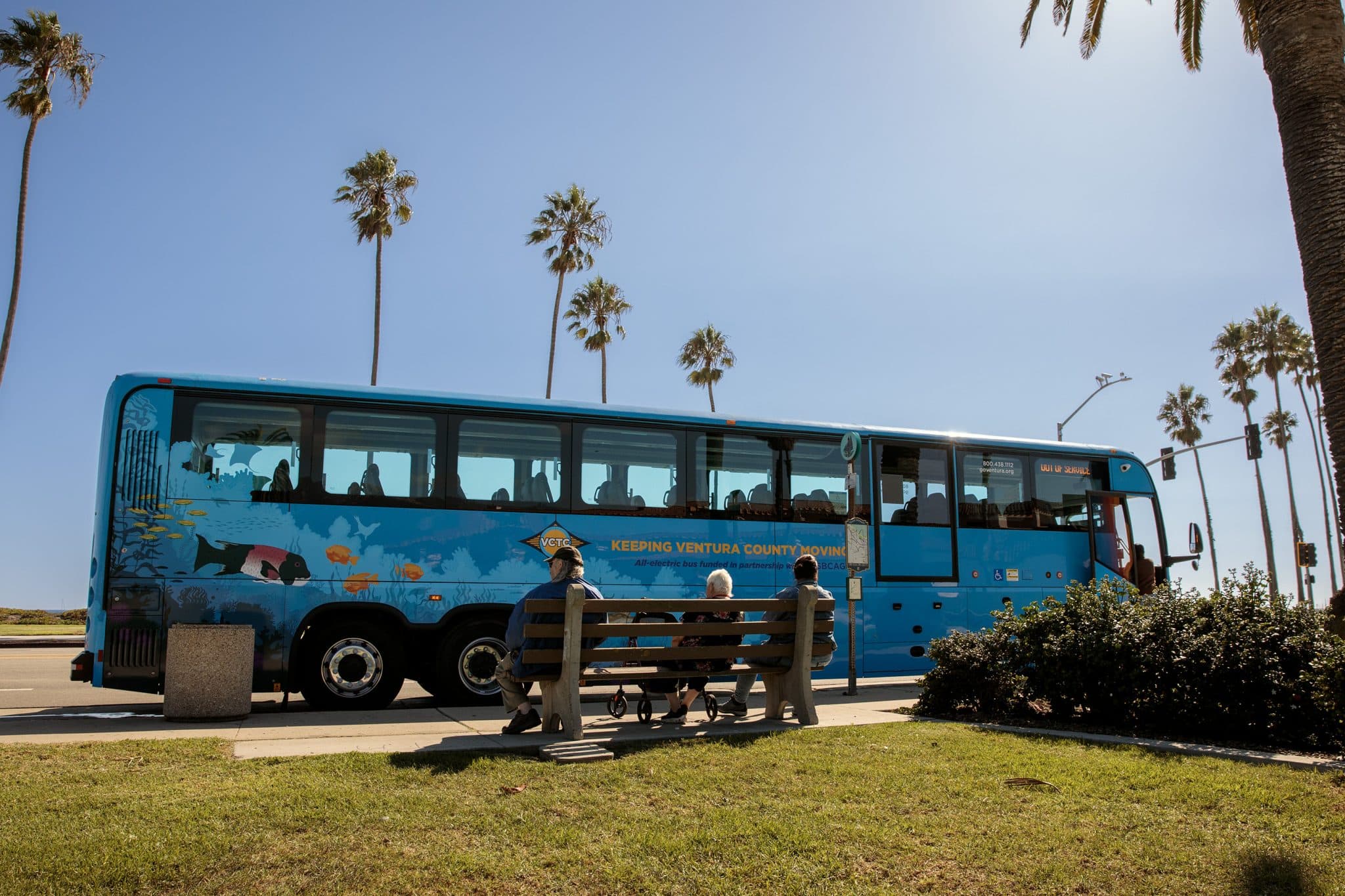People sitting on a bench with VCTC parked on the road in the background