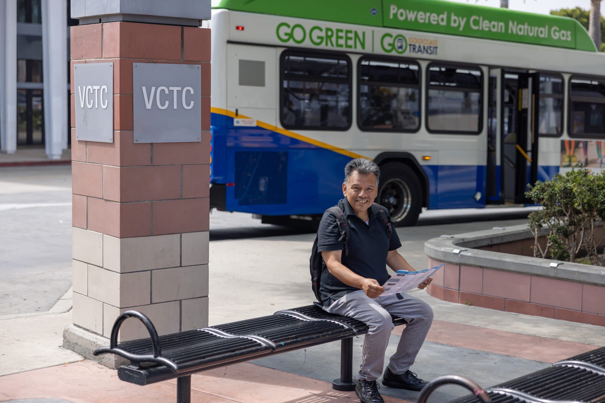 Man sitting at bus stop holding his phone with bus in the background