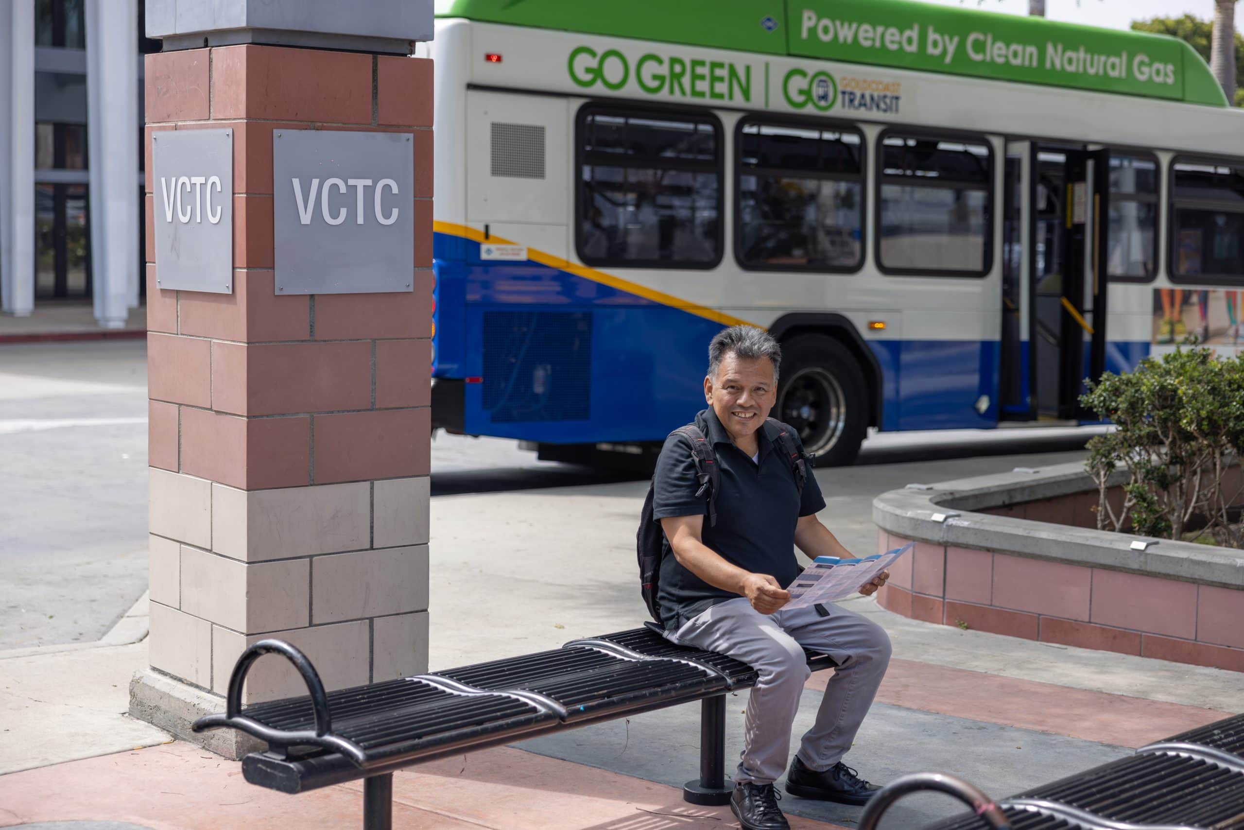 Man sitting at bus stop holding his phone with bus in the background